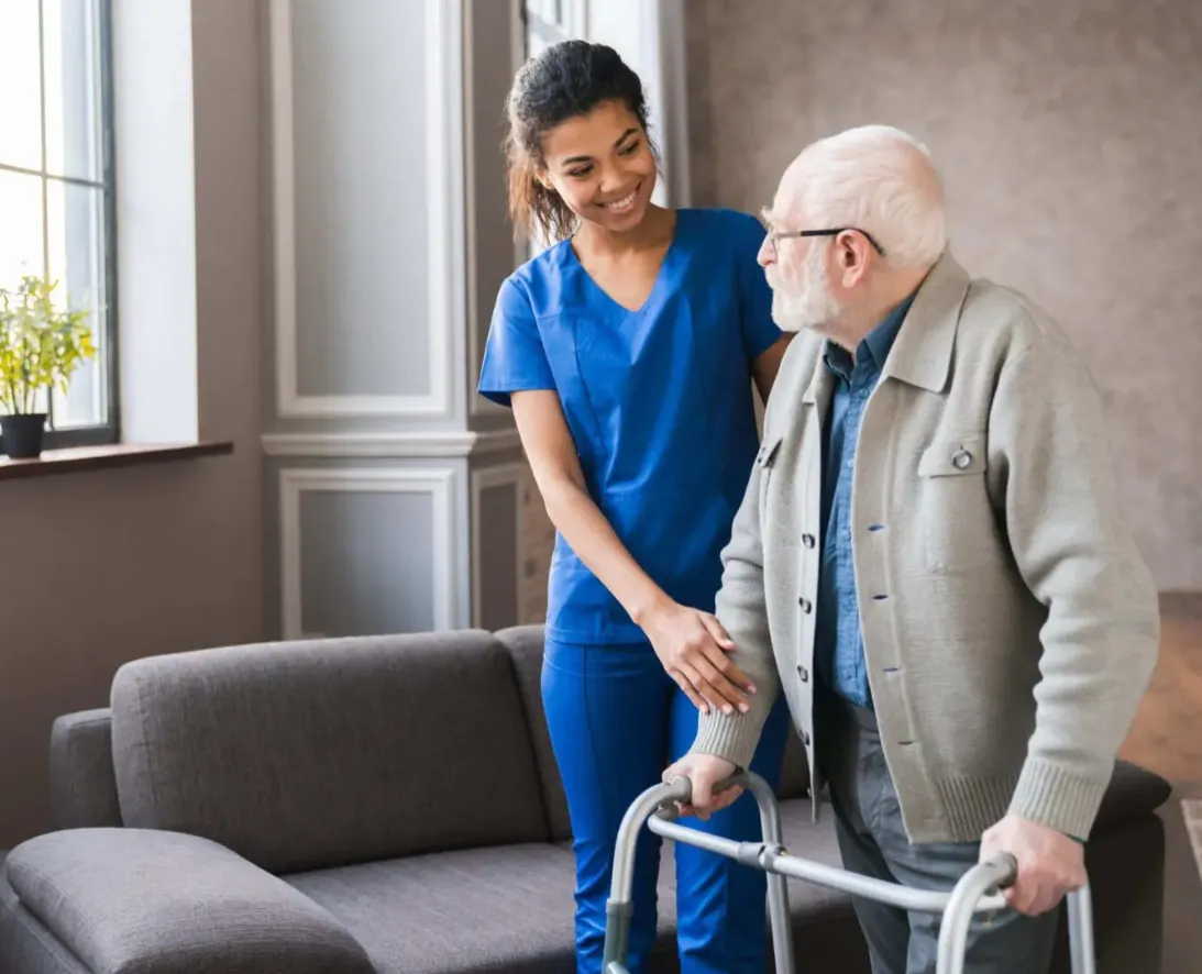 A caregiver helping an older man steady himself with a walker